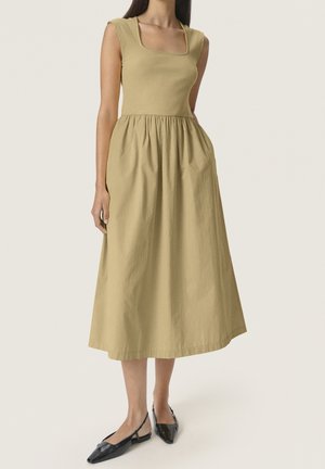 Sukienka khaki w kształcie litery A z prążkowanym gorsetem, kwadratowym dekoltem i marszczonym dołem, zestawiona z czarnymi lakierowanymi butami na obcasie z odkrytą piętą.