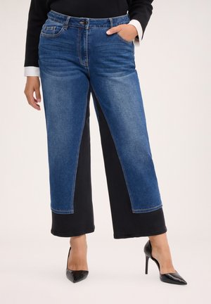 Persona que lleva pantalones de pierna ancha con paneles delanteros de denim azul y paneles traseros de tela negra, combinados con zapatos de tacón negro.