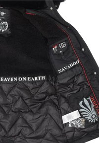 Wnętrze czarnej pikowanej kurtki puchowej z pikowanym wzorem, sztucznym futerkiem, czerwonym przeszyciem, wieloma kieszeniami oraz nadrukowanymi detalami z logo.