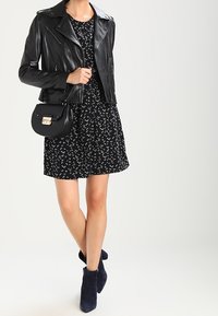 Czarna skórzana kurtka motocyklowa na krótkiej czarnej sukience z białym wzorem, w połączeniu z granatowymi botkami sięgającymi kostki i małą czarną torebką.