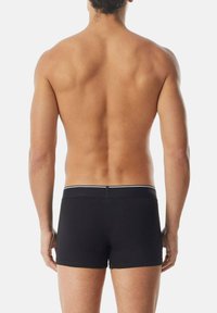 Svarta boxershorts med ett vitt midjeband, med en mjuk tygtextur och en skräddarsydd passform, sedd bakifrån mot en neutral bakgrund.