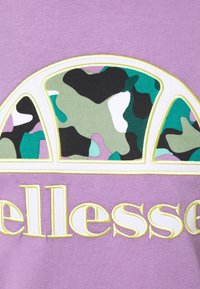 Lila bomullströja med en stor bågeapplikation i camouflage-design i gröna, svarta och lila nyanser, accentuerad med vit och gul sömnad.