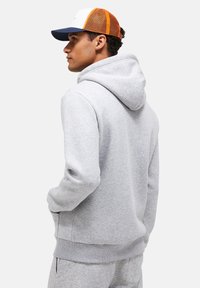 Gray hooded sweatshirt with a soft texture, ribbed cuffs, and hem. Paired with a cap featuring a white front, orange mesh back, and navy brim.