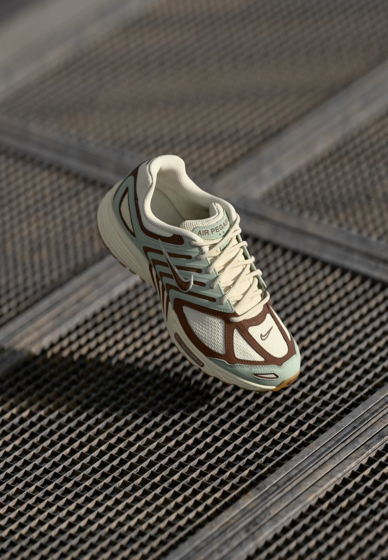 Baskets Nike Air Pegasus en crème, marron et vert menthe. Présente des panneaux en maille, une semelle texturée et des accents contrastants dans son design.
