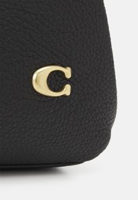 Czarny teksturowany materiał skórzany z małą złotą metalową literą "C" zdobioną w pobliżu dolnej krawędzi.
