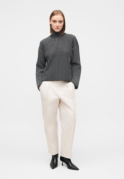 Πουλόβερ ζιβάγκο με ασπρόμαυρες ρίγες, άνετη εφαρμογή· κρεμ παντελόνι ψηλόμεσο· μαύρες μυτερές γόβες. Ομαλές υφές και κομψός σχεδιασμός.