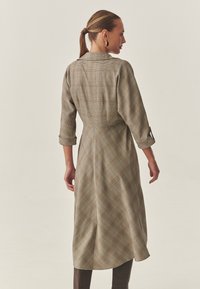 Abito lungo a quadri in tonalità terrose miste, con scollo con colletto, maniche a tre quarti e vita increspata, caratterizzato da dettagli a strisce diagonali.