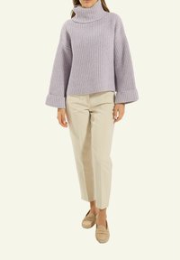 Lavenderfarbener, gerippter Strickpullover mit hohem Kragen und weiten Ärmeln, kombiniert mit beigefarbenen, maßgeschneiderten Hosen und hellbeigen Slippern.