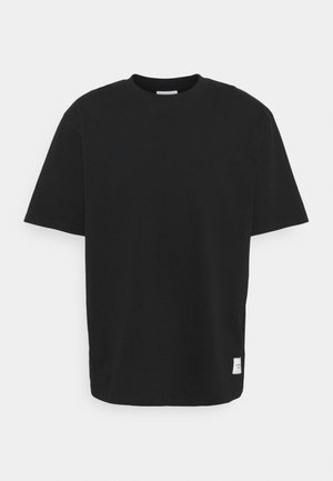 Crna majica s okruglim izrezom, kratkim rukavima i ravnim krojem. Izrađena od mekog pamuka, sadrži malu oznaku na donjoj lijevoj strani.