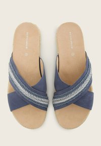 Chinelas bleu marine avec un accent en argent tressé, en suède doux, et une semelle intérieure en tan rembourrée. Design léger et ouvert.