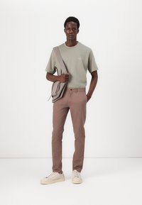 Camiseta verde claro de manga corta, pantalones marrones de corte slim, zapatillas crema y bolso gris de hombro. Diseño simple con mínima marcas.