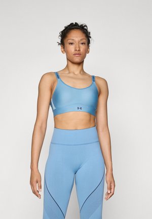 Lyseblå sports-bh med elastiske stropper som har et logo, paret med matchende høyhøydede leggings med teksturert sidelayout.