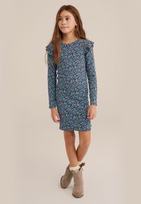 Dolga rokava, prilegajoča obleka v temno modri barvi z cvetličnim vzorcem v beli, zeleni in vijolični barvi. Vsebuje volančke na ramenih.