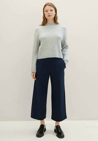 Suéter canelado cinza claro com gola alta, combinado com calças largas azul-marinho e sapatos pretos com atacadores. O conjunto tem um ajuste descontraído.