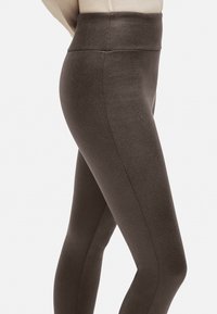 Leggings de cintura alta en marrón oscuro, con una superficie lisa y texturizada y costuras laterales para una silueta ajustada.