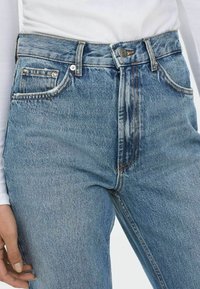 Hoge taille blauwe denim jeans met vijf zakken, koperen stiksels en een licht vervaagde textuur, met een metalen knoopsluiting.