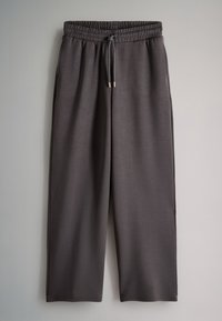 Pantaloni larghi grigio scuro con elastico in vita e coulisse appesi su sfondo chiaro.
