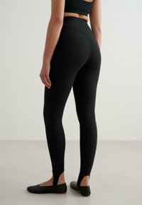 Svarta höga leggings med ett mjukt, elastiskt tyg. Har sidokutade öppningar vid anklarna och en åtsittande design. Bärs med svarta ballerinaskor.