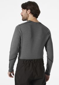Grijze lange mouwen shirt met gestructureerde stof, voorzien van een ronde halslijn en zwarte accentnaden, gecombineerd met donkere, elastische taillebandbroeken.
