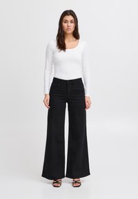 Fekete, széles szárú farmernadrág magas derékkal és elülső zsebekkel, fehér, testhez simuló hosszú ujjú felsővel párosítva.