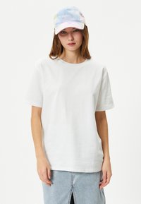 Vit bomull t-shirt med korta ärmar, rund halsringning, tillsammans med en pastellfärgad tie-dye keps med broderad text.