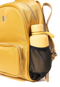 Žlutý batoh s přední kapsou na zip a černou síťovanou boční kapsou, ve které se nachází odpovídající žlutá láhev na vodu se strapcovým víkem.