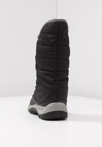 Botte noire isolée avec une texture matelassée et une semelle en caoutchouc grise. Présente un haut chaussant et un orteil arrondi pour plus de chaleur et de soutien.