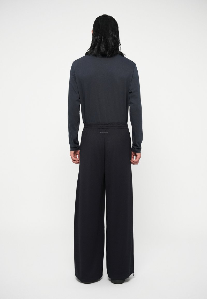 Maglietta a maniche lunghe grigia scura abbinata a pantaloni neri a gamba larga, con tessuto testurizzato e vita elasticizzata, vista da dietro.