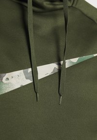 Sweat-shirt à capuche vert avec une bande d'accent en imprimé camouflage. Il possède des cordons plats et un tissu texturé et doux.