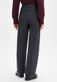 Wide-leg trousers in dark gray with pinstripe pattern. Smooth texture, high waist, and two back pockets. Black chunky shoes visible.