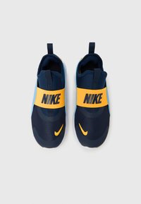 Baskets bleu et marine avec une empeigne texturée, dotées d'une bride et d'un accent Nike jaunes. Conçues sans lacets pour un enfilage facile.