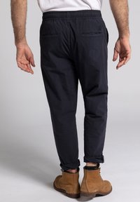 Pantalones azul marino con cinturilla elástica y puños doblados, que cuentan con dos bolsillos traseros y una textura suave. Combinados con botas de tobillo marrones.