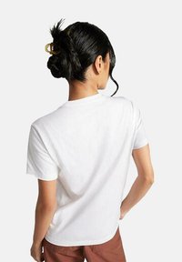 Camiseta blanca de algodón con mangas cortas y cuello redondo. La espalda es lisa y tiene un corte relajado. Sin patrones ni diseños visibles.
