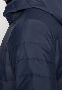 Námořnická pufovaná bunda se vyznačuje prošívaným designem s horizontálním švem, kapucí a hladkým povrchem. Vhodná pro chladné počasí.