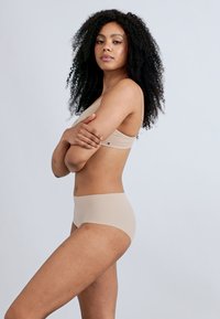 Μπεζ μπουστάκι χωρίς ραφές και ταιριαστό σλιπ, ελαστικό ύφασμα, μινιμαλιστικός σχεδιασμός, λεία υφή, εφαρμοστό κόψιμο με ζώνη στη μέση.