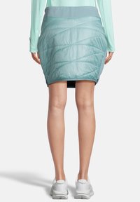 Falda aislante de color teal claro con un patrón acolchado y una cinturilla ancha. Fabricada con un material suave y brillante; cuenta con un forro interno negro.