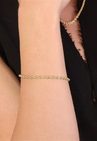 Gold-tone bracelet with a twisted design, featuring a smooth surface and a round shape, worn on a bare wrist against a dark background.