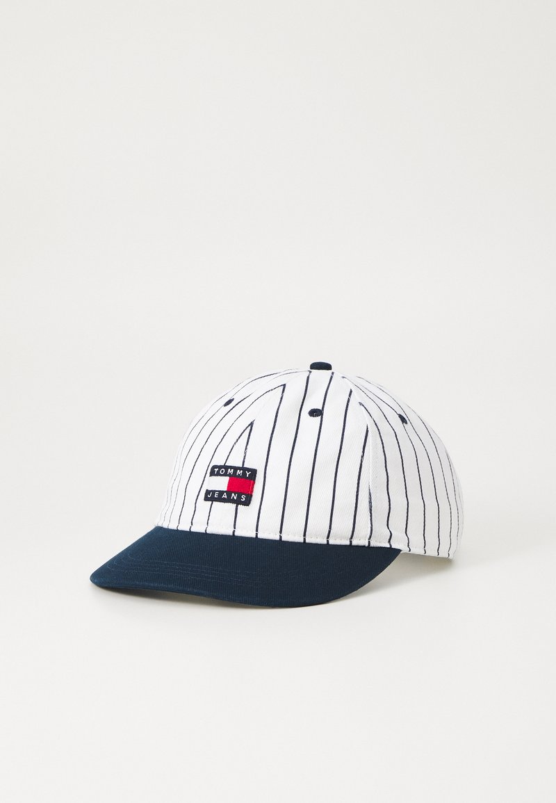 White baseball cap with navy brim, pinstripe design, and a red and black "TOMMY JEANS" logo patch on the front. Cotton material.