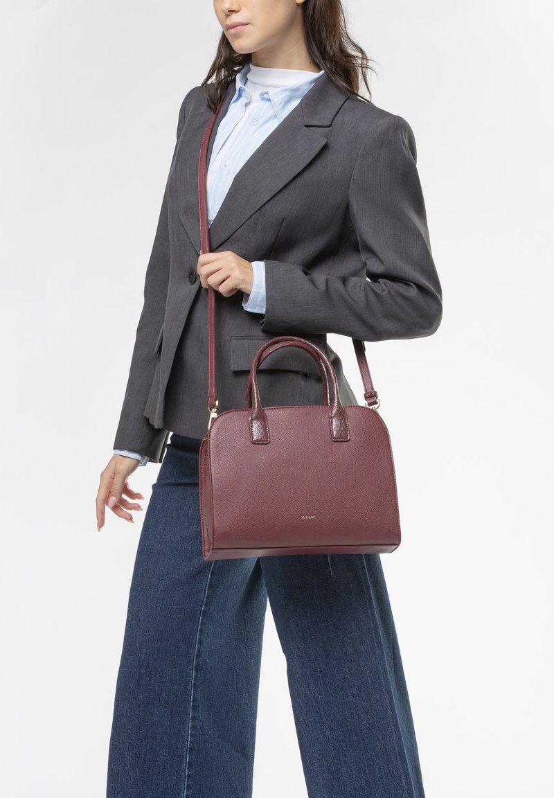 Borsa a mano in pelle bordeaux con doppi manici, tracolla removibile e forma strutturata. Texture liscia, dettagli del logo discreti sul davanti.