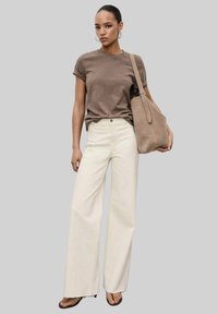 Brown short-sleeve cotton t-shirt paired with high-waisted, wide-legged cream trousers. Model carries a beige suede handbag.