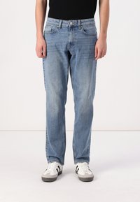 Lyseblå denimjeans med rett snitt, fem lommer og synlige sømdetaljer, brukt med hvite sneakers med svarte akcenter.