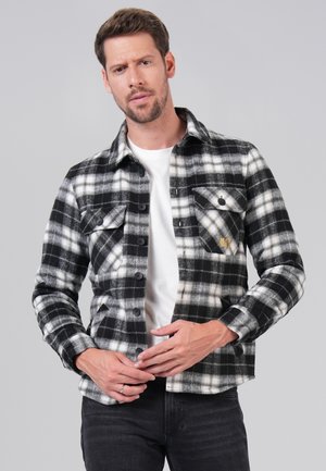 Black and white plaid shirt with button-up front, two chest pockets, and a textured fabric. Worn over a white T-shirt and dark jeans.