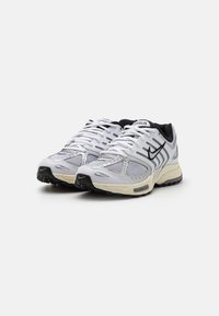 Pár bílých a šedých běžeckých bot Nike s černými akcenty a síťovinovými panely, umístěných vedle sebe na bílém pozadí.