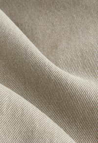 Light beige fabric with a subtle diagonal weave pattern, featuring a soft texture and a slight sheen, draping naturally in folds.