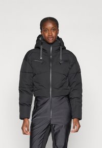 Must värviline pehme talvemantel kõrge kaelusega, kahe lukuga rinnataskuga ja reguleeritavad nöörid kapuutsil. Sile kangast tekstuur.