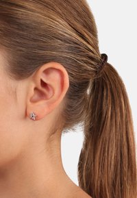 Silberne sternförmige Ohrringe mit bunten Edelsteinen, die am Ohr eines Models mit einem schlichten Pferdeschwanz präsentiert werden.