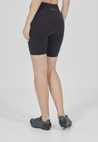 Svarta cykelbyxor med hög midja, vadderad sits och slät tyg. Bärs med svarta cykelskor som har en säker remdesign.