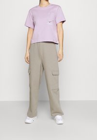 Lila kortärmad t-shirt med en framficka och Nike-logotyp. Matchas med ljusgrå cargobyxor med sidofickor. Vita sportskor.