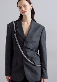 Gray wool blazer with a tailored fit, featuring two buttons, pocket details, and a silver chain accent draping across the front.