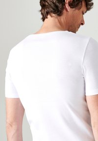 T-shirt bianco a maniche corte realizzato in morbido cotone, con scollatura a girocollo e design aderente, mostrato di spalle con texture liscia.
